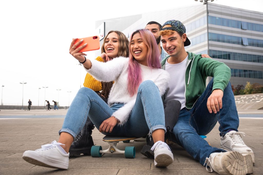 Happy teen friends taking a selfie sitting on a skateboard