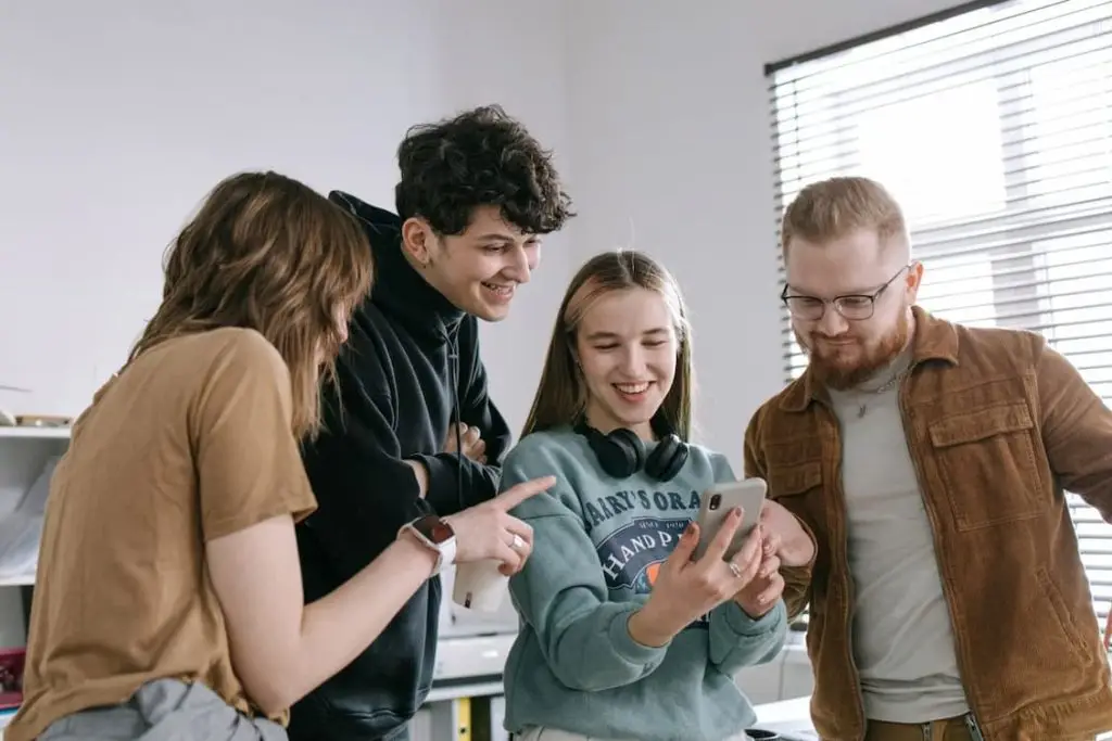 group-of-people-smiling-while-looking-at-woman-s-mobile-phone